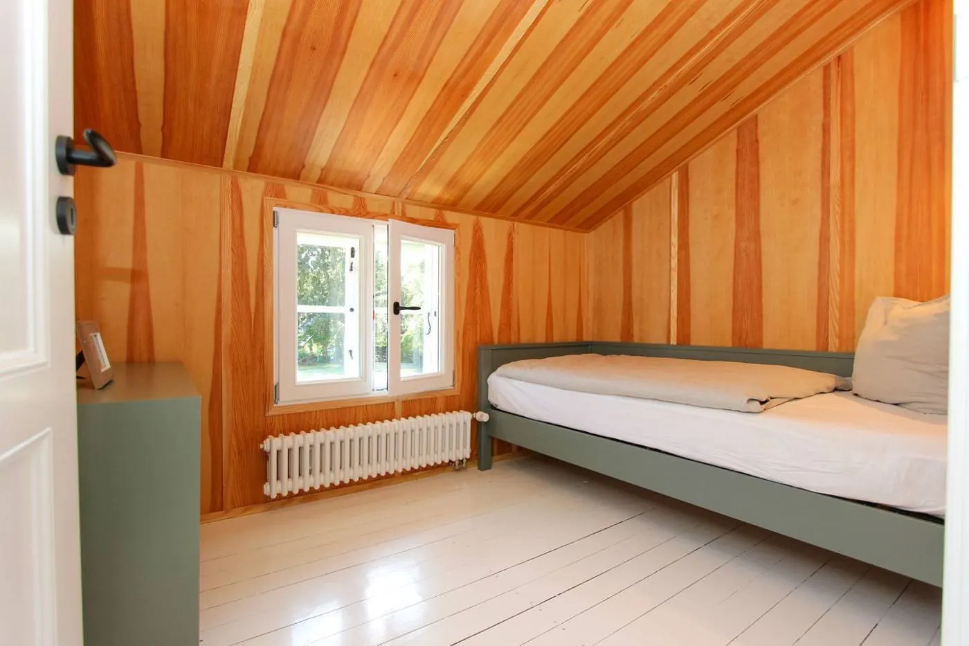 Holzverkleidetes Zimmer mit Einzelbett in Salbeigrün und Fenster