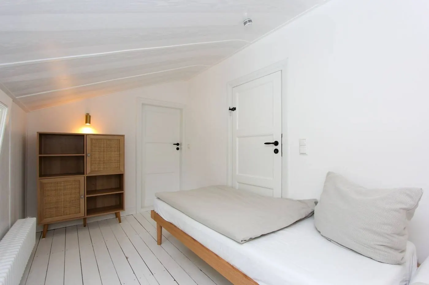 Weiß gestrichenes Dachzimmer mit Einzelbett, Rattanschrank und zwei Türen
