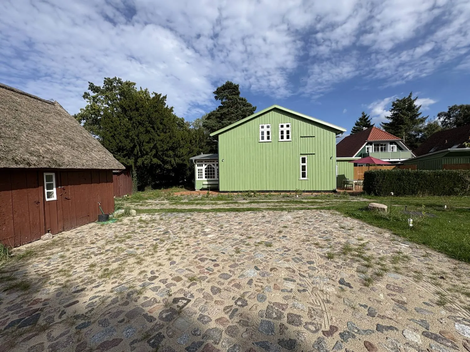 Ferienhaus Prerow: gepflasterter Hof mit Parkplätzen aus Natursteinen, rechts die Wiese, dahinter das grüne Haus