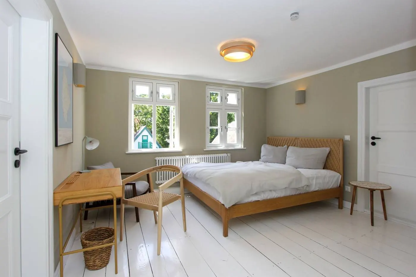 Helles Schlafzimmer mit Doppelbett, Holzschreibtisch und zwei Sprossenfenstern