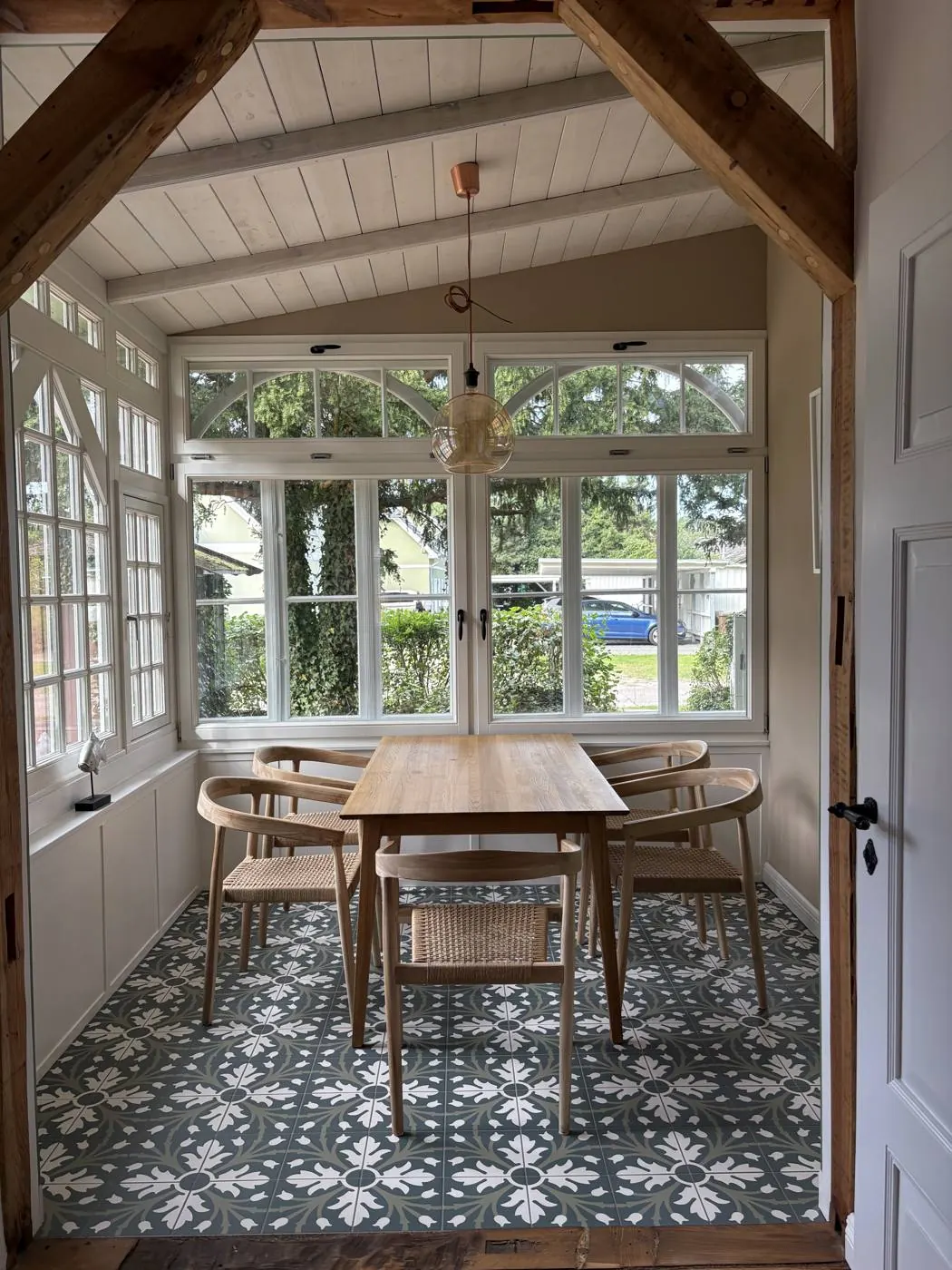 Veranda mit Holzbalken, großen Sprossenfenstern, Esstisch mit Stühlen und gemustertem Fliesenboden