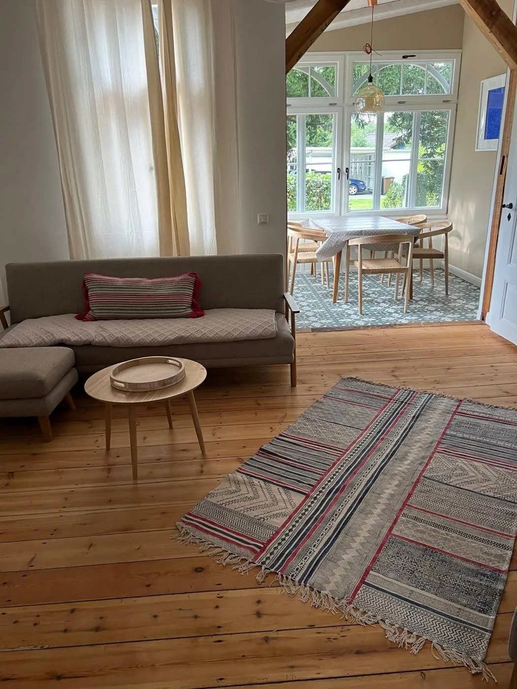 Sofa, Rundtisch und Teppich, dahinter die Veranda mit großen Sprossenfenstern