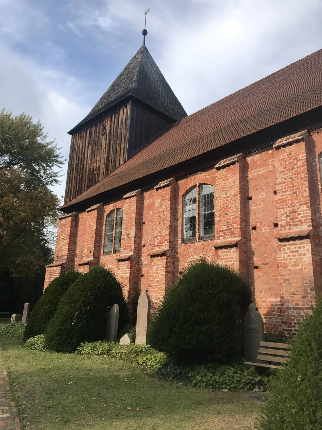 Rote Backsteinkirche mit hölzernem Turm und Friedhof